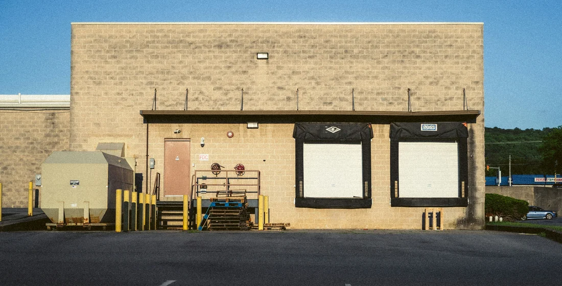 A warehouse elevation with two dock openings and a wide empty asphalt apron running away from it