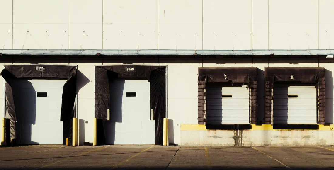 A row of loading dock doors with black dock shelters along a warehouse elevation, with an open concrete apron in front