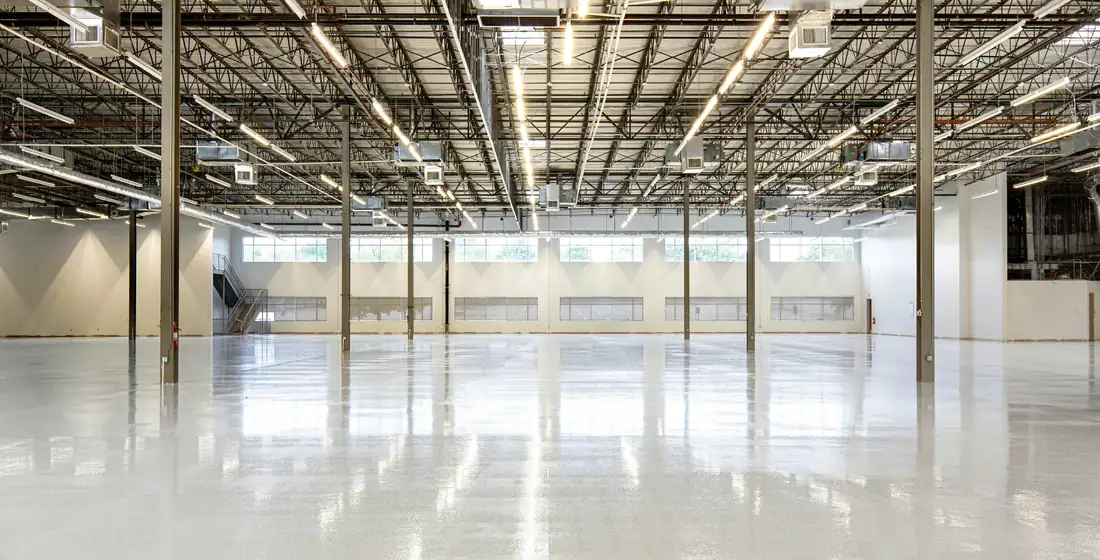 Wide empty warehouse interior with a bare concrete floor and daylight along one side