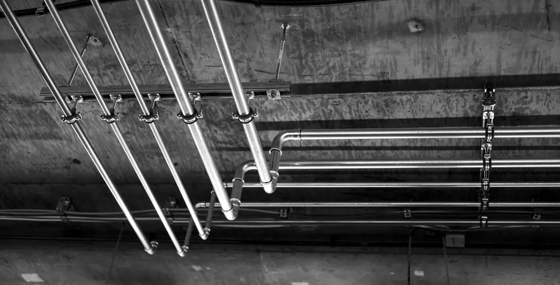 Conduit and pipe runs fixed across a concrete ceiling inside an industrial building