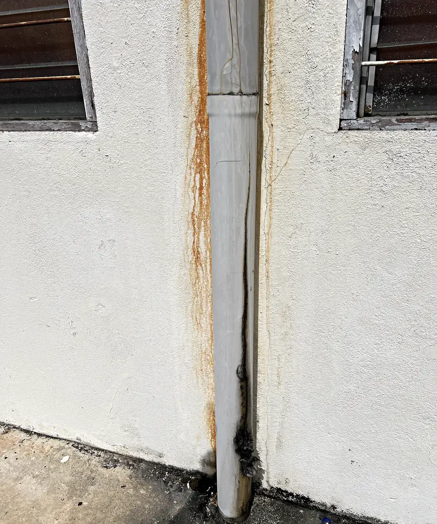 External downpipe between two louvre windows with water staining running down the rendered wall