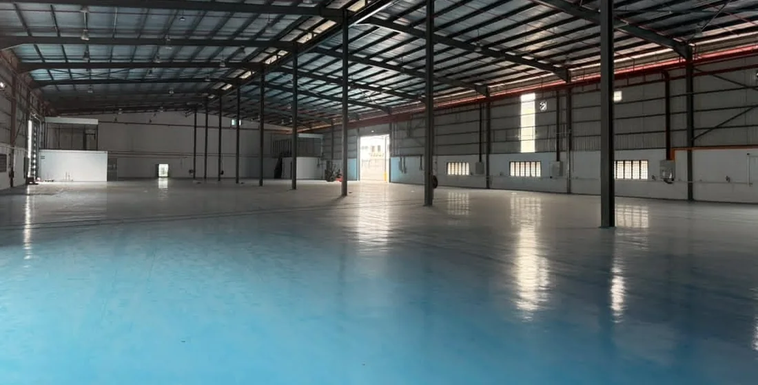 Large empty warehouse with a blue coated concrete floor reflecting the roof lights