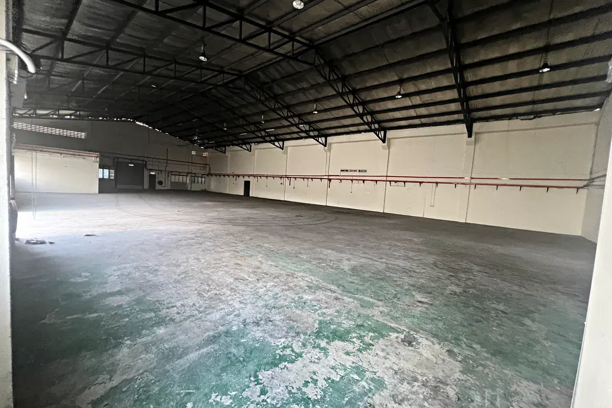 Bahagian dalam bangsal kilang yang besar dengan kerangka portal keluli dan seorang berdiri sebagai skala