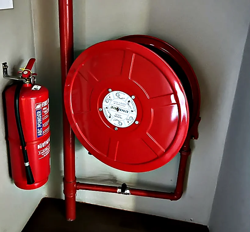 Fire extinguisher and red hose reel mounted in the corner of a building, fed by a red riser pipe