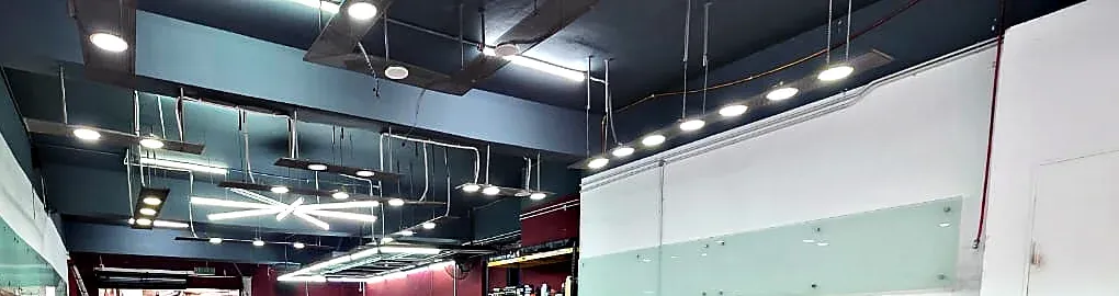 Ducting, conduit and trunking run on the surface below a shop unit soffit, with mixed lighting types