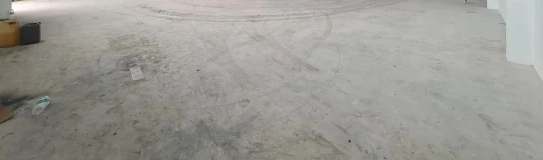 Bare uncoated concrete warehouse floor with tyre tracks across it