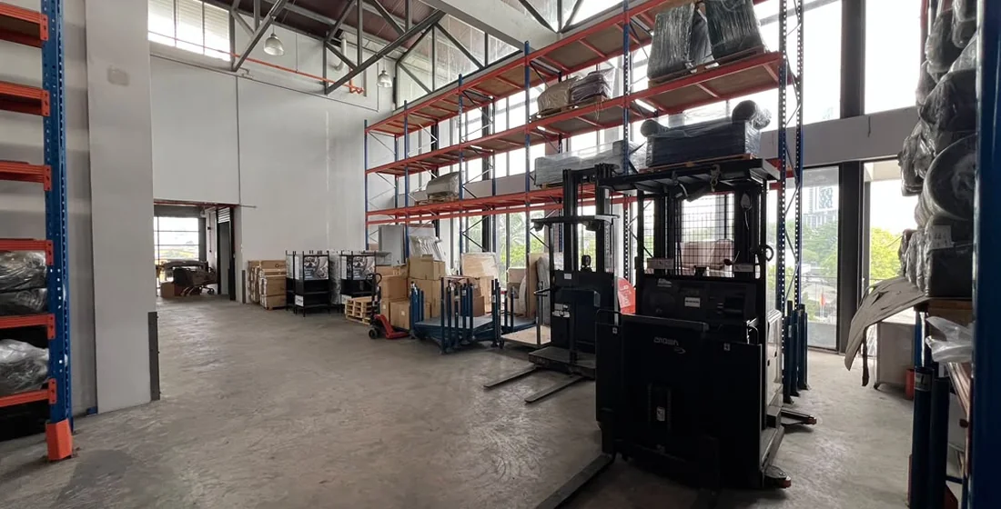 Warehouse interior with loaded pallet racking on both sides, a reach truck standing in the aisle, and bare concrete floor across the foreground
