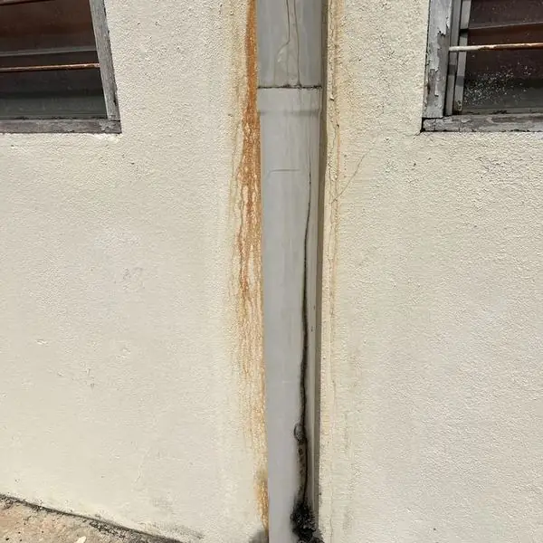 Cracked rainwater downpipe with rust staining running down the external wall below it