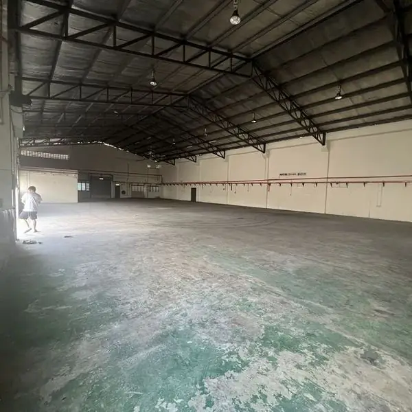 Interior of a vacant factory unit showing a steel truss roof and open concrete floor